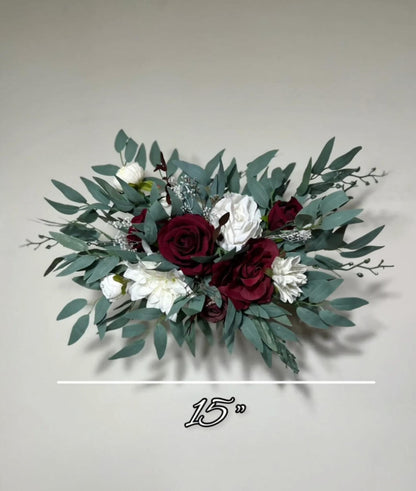 A bouquet of red roses, white flowers, and green leaves is displayed against a plain background.