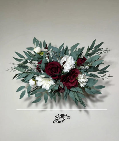 A bouquet of red roses, white flowers, and green leaves is displayed against a plain background.